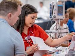 Woman wearing red scrubs, holding papers, talking to man.